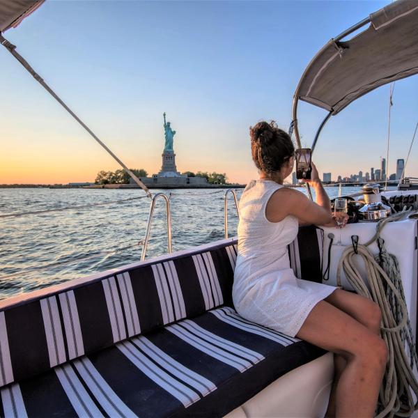 woman in a white dress facing the Statue of Liberty to take a photo during a private boat tour New York