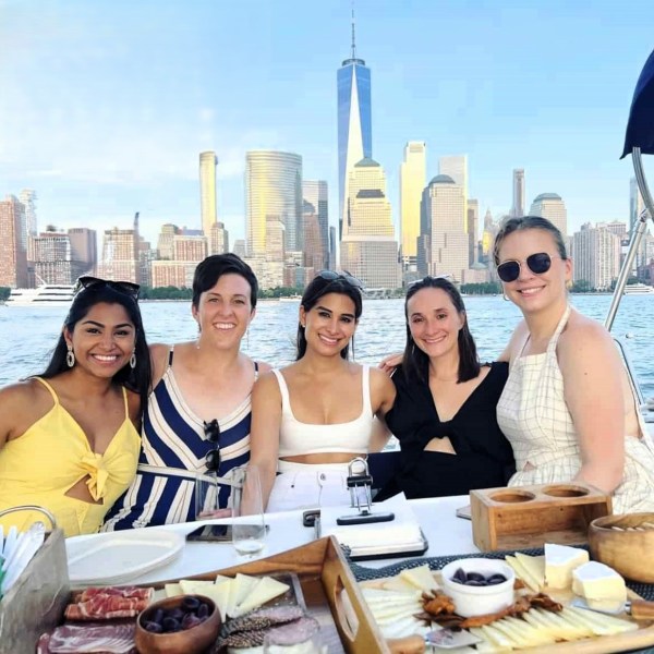 women on a boat ride NYC with dinner and the NYC skyline and One World Trade Center in the background during a boat rent NYC