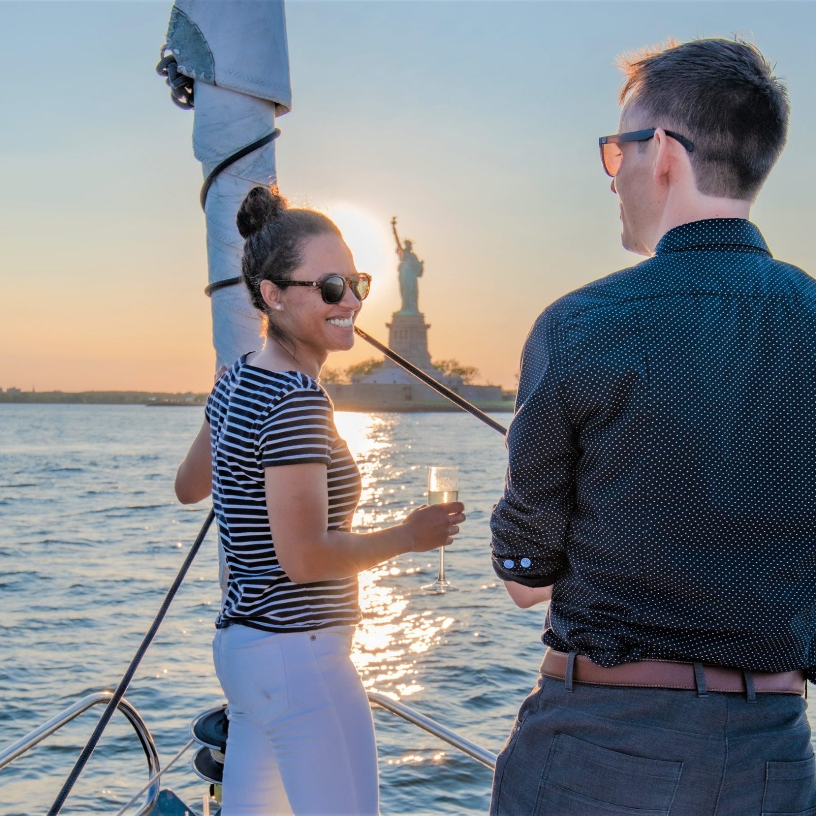 woman and man facing each other with the Statue of Liberty in the background during a private sailing charter NYC