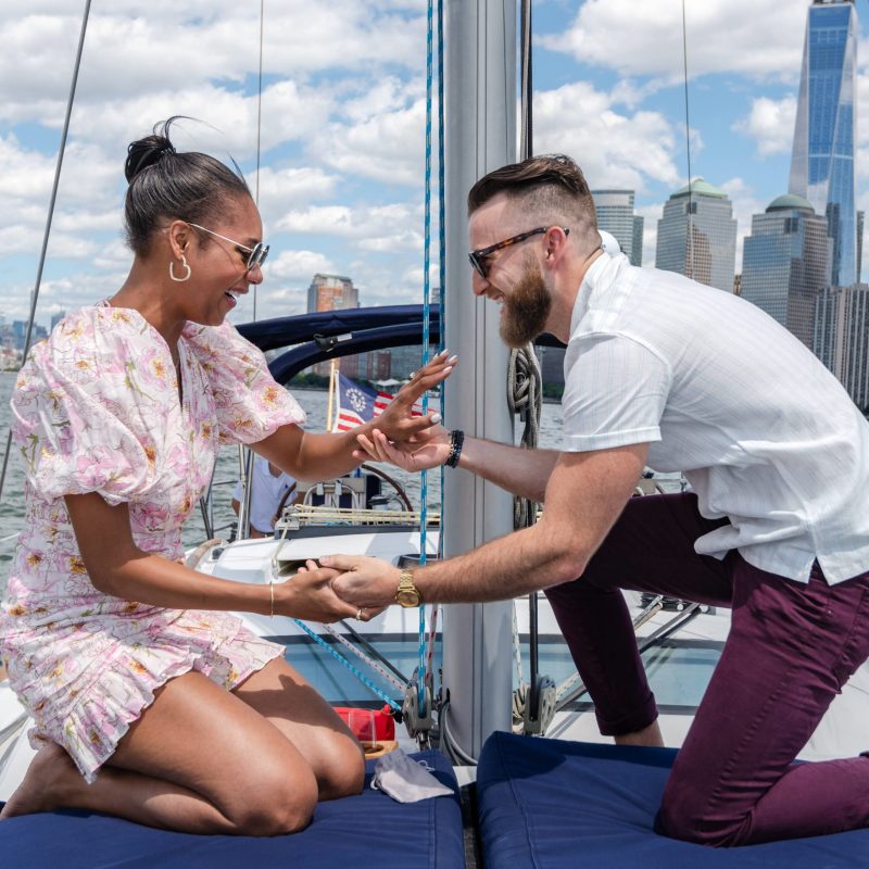 man and woman kneeling on blue cushions during a boat proposal in NYC