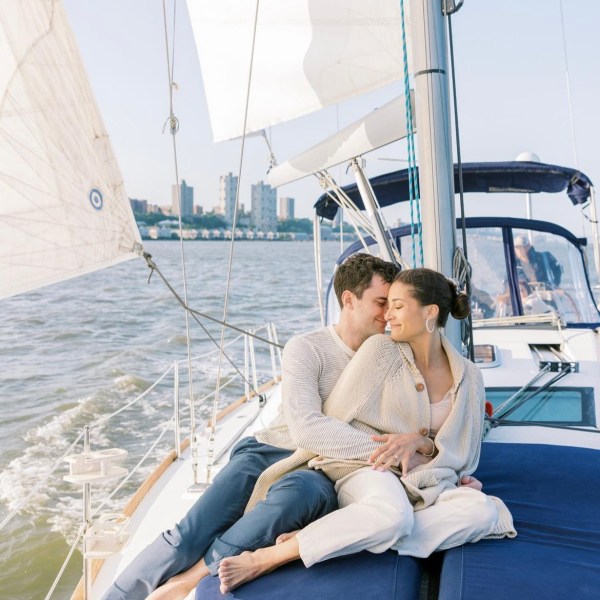 couple on a NYC romantic boat ride sitting on blue cushions with white sails in the background