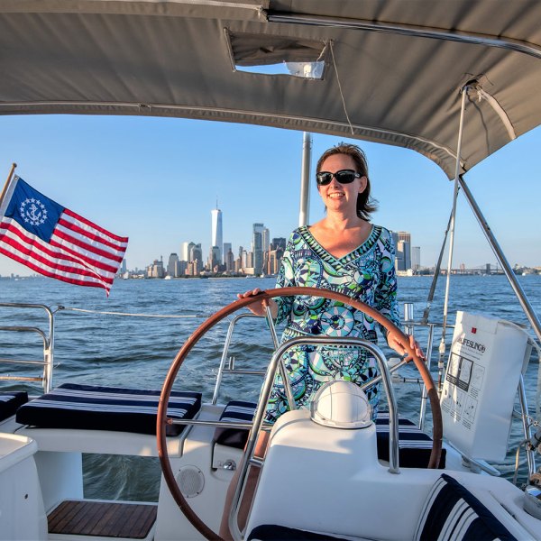 woman in paisley dress and sunglasses behind the wheel of a New York private boat charter