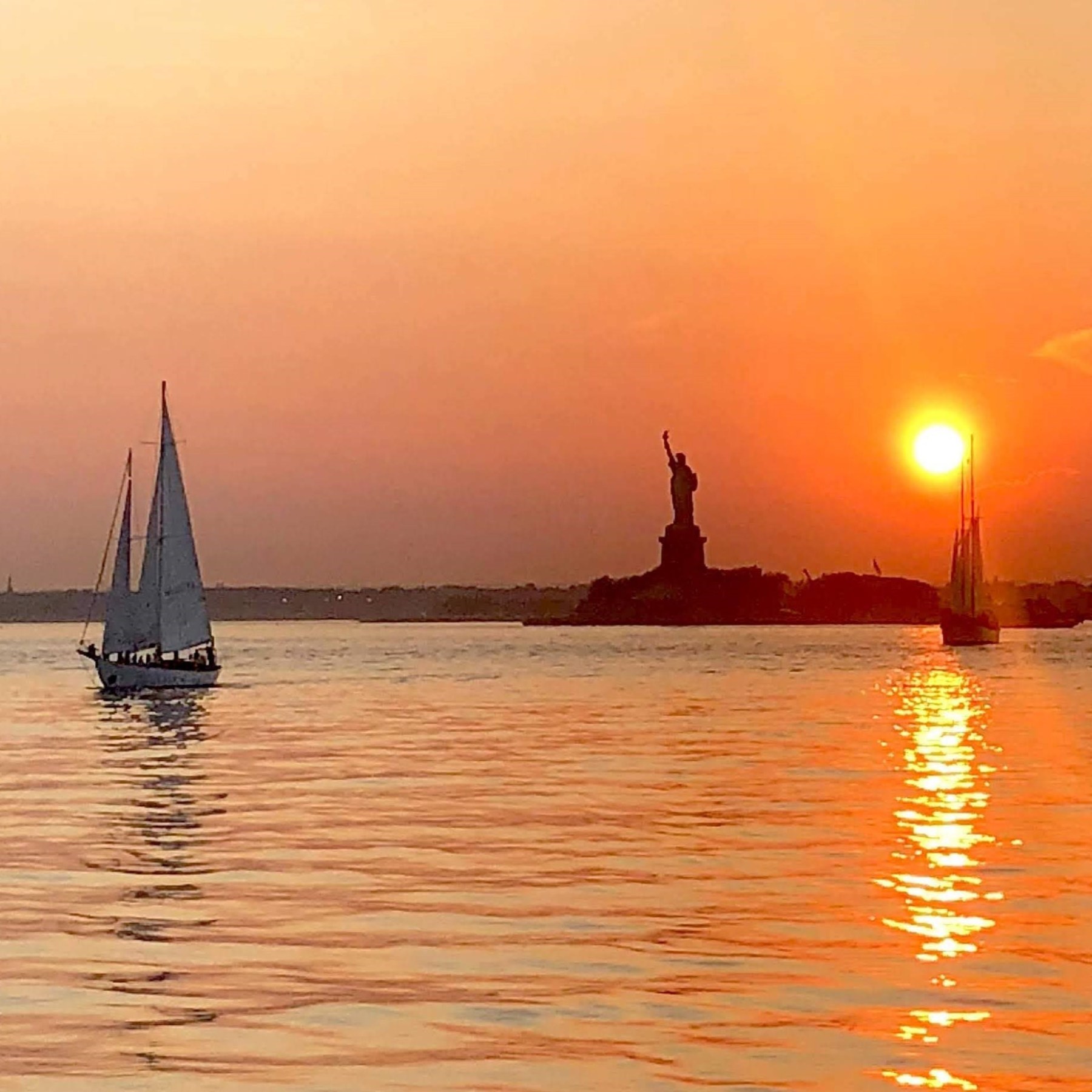 sunset sailboat cruise with an orange sky reflected of the water in NYC with the Statue of Liberty in the background