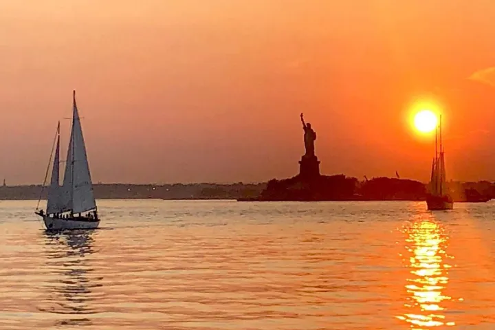 sunset sailboat cruise with an orange sky reflected of the water in NYC with the Statue of Liberty in the background