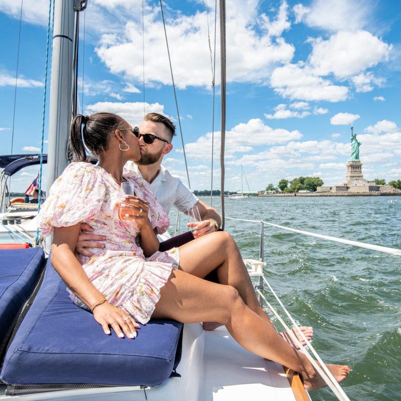 couple kissing on a romantic boat rental in NYC with the Statue of Liberty behind them