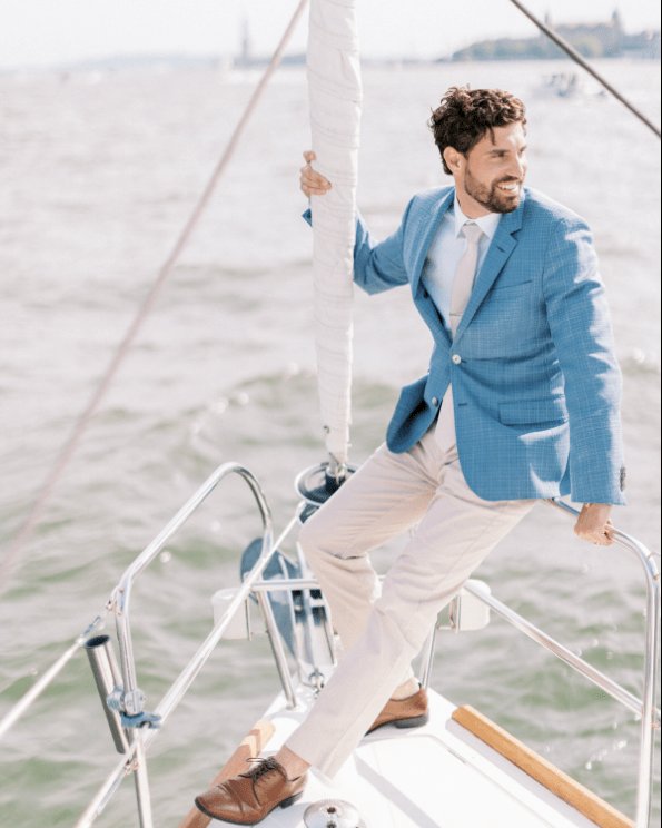 man in a blue jacket sitting at the bow of a boat holding a furled sail during a private boat ride in NYC