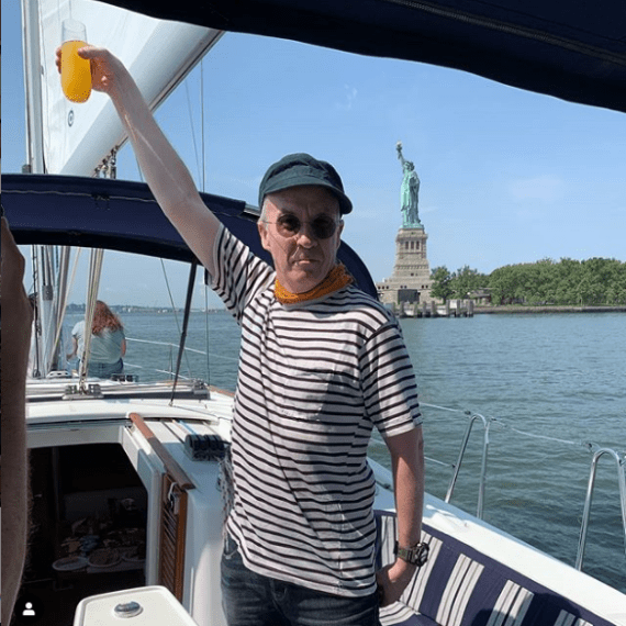 a man holding a mimosa next to the Statue of Liberty during a brunch cruise in NYC