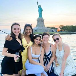 Five women on a boat rental smiling and enjoying a private Statue of Liberty boat tour at sunset with close-up views