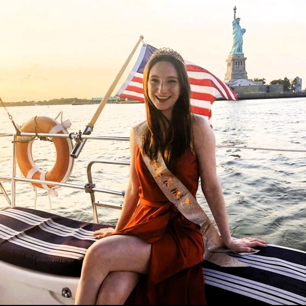 birthday girl with sash and American flag and orange buoy on a rent a yacht in NYC with the Statue of Liberty in the background