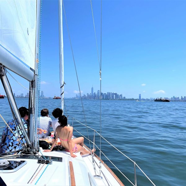 friends sunbathing during a private sailboat charter of NYC with the Manhattan skyline ahead