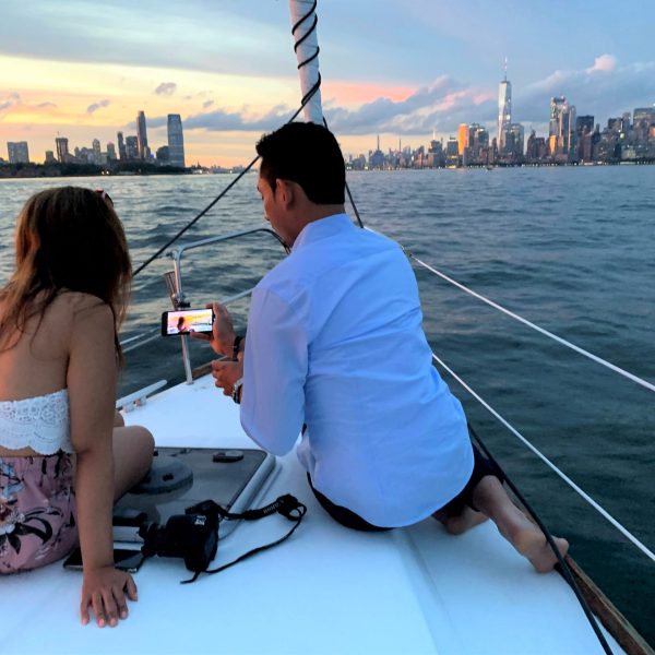 couple looking at photos on their phone while sailing the New York Harbor at sunset