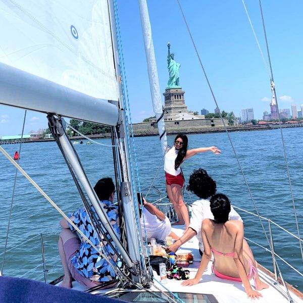 woman standing on the bow of the boat with her hands up in front o the Statue of Liberty during a sail boat ride NYC