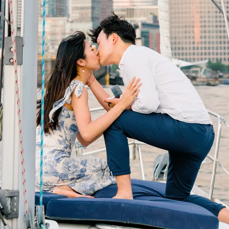 man and woman kiss during a boat proposal in NYC with the NYC skyline in the background