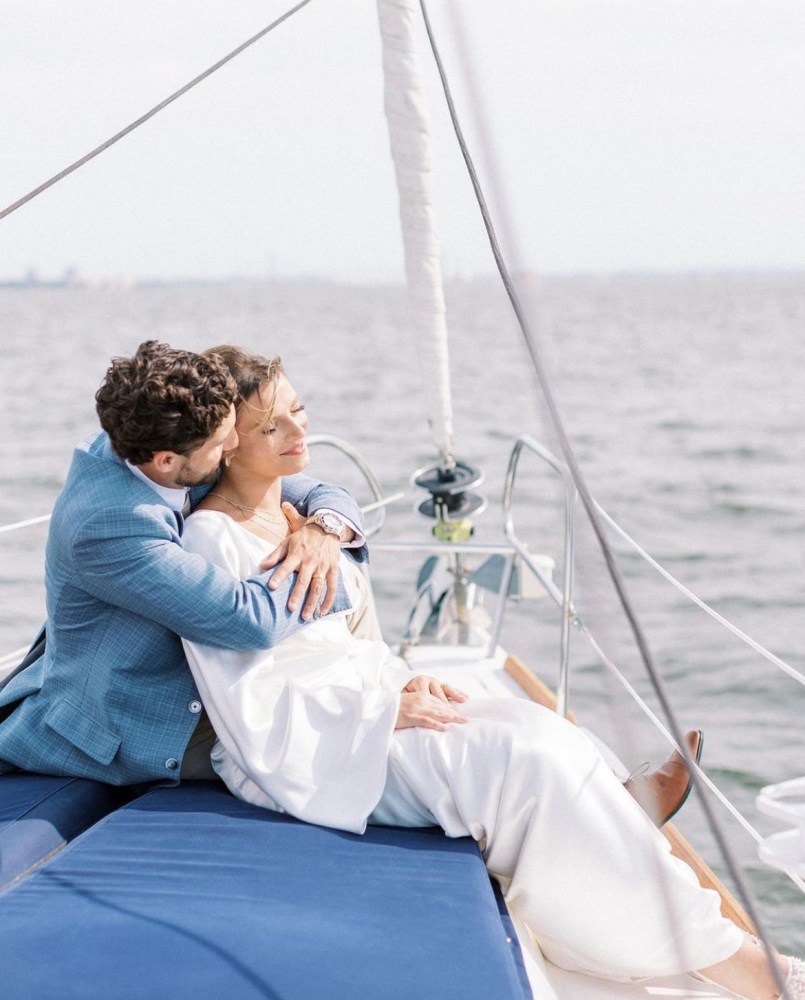 man in blue suit and woman in white dress sitting on a blue cushion during a boat charter NYC