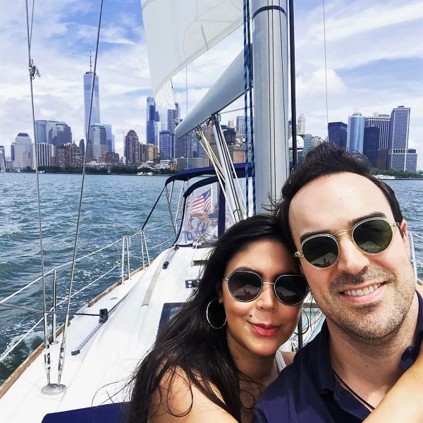 a woman and man wearing sunglasses on the deck of a private sailboat charter NYC with the World Trade Center and Manhattan skyline in the background
