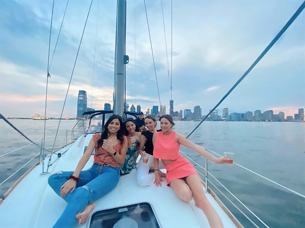 4 women on deck with the Manhattan skyline in the distance while on a sailing cruise of NYC