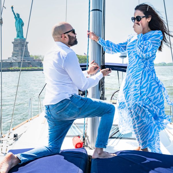 man kneeling in front of a woman in a blue dress during a statue of liberty proposal