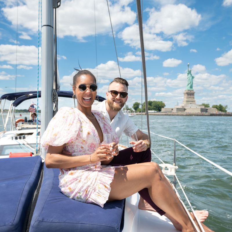 couple sitting on the deck of a boat with the statue of liberty behind them during a romantic boat ride for 2