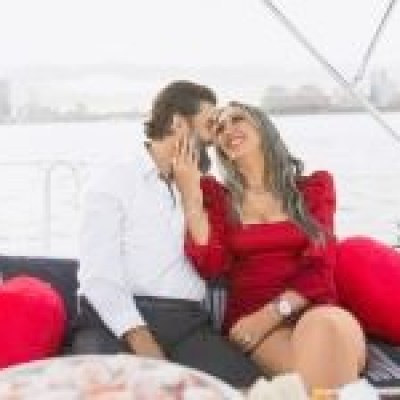 couple smiling on a romantic boat rides in the NY Harbor with red heart pillows on the seats