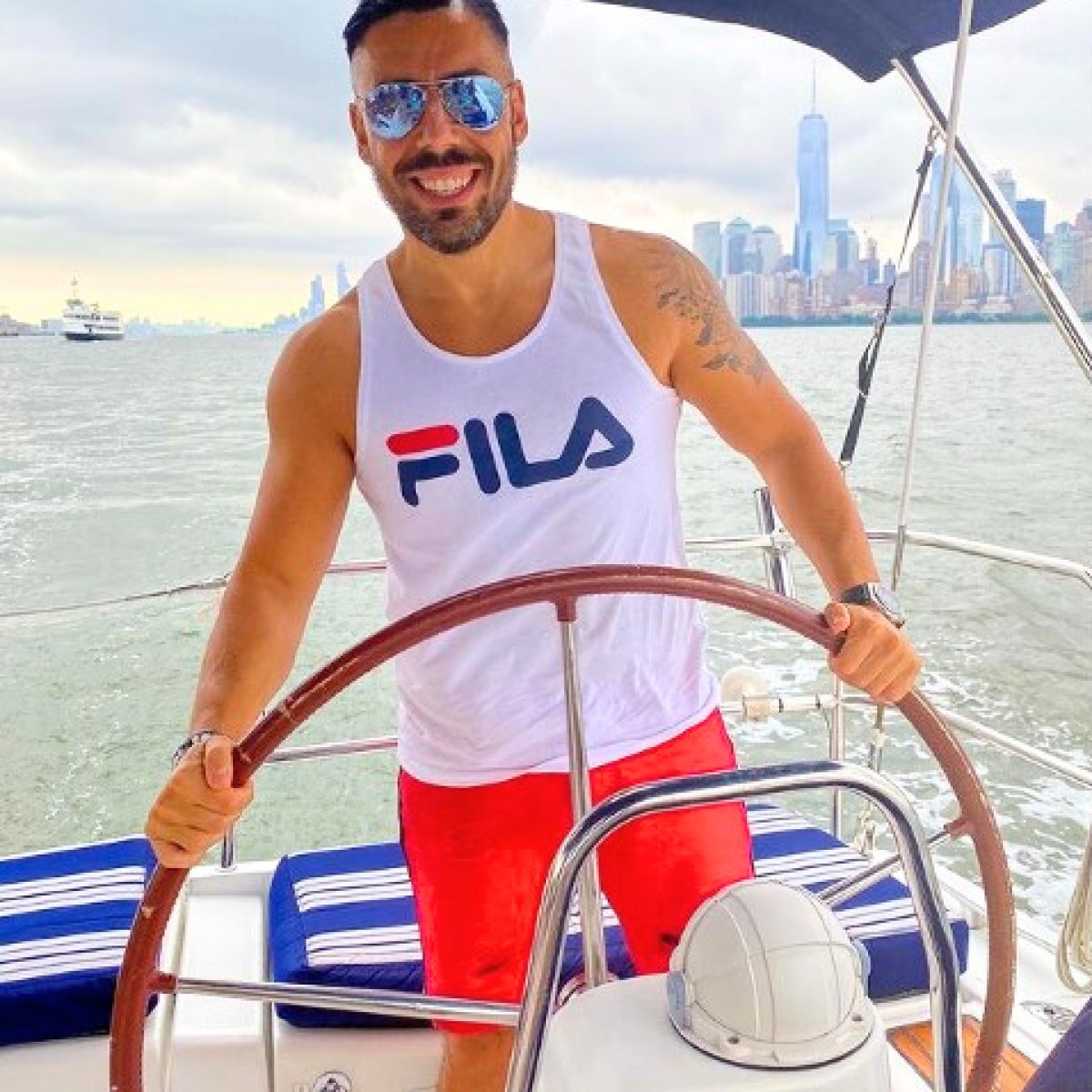 man wearing red shorts and FILA shirt behind the wheel of a boat rental in New York