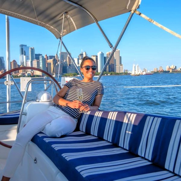 woman sitting on blue striped cushions with the Manhattan skyline behind her on a private boat charter in NYC.