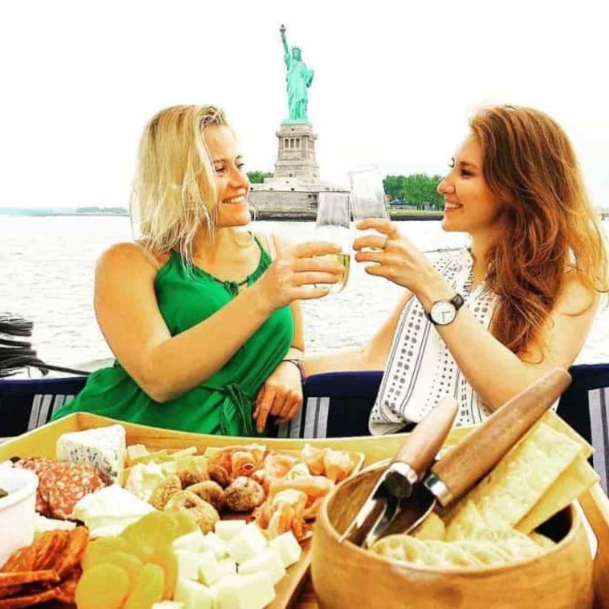 two women toasting glasses with champagne by the Statue of Liberty on a luxury boat rental in NYC