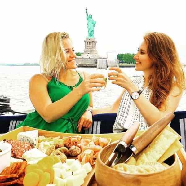 two women toasting glasses with champagne by the Statue of Liberty on a luxury boat rental in NYC