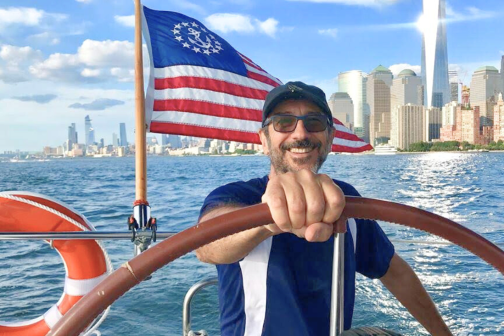 captain at the helm of a boat rental in New York with the American flag and Manhattan skyline in the background