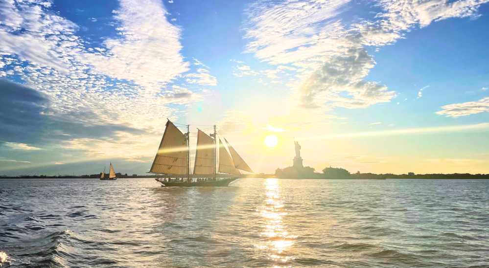 sailboat sailing to the Statue of Liberty at sunset with a charter a boat in NYC