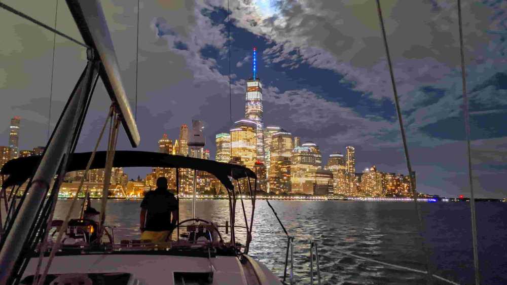 Boat rental at night with view of illuminated NYC skyline and clouds overhead.