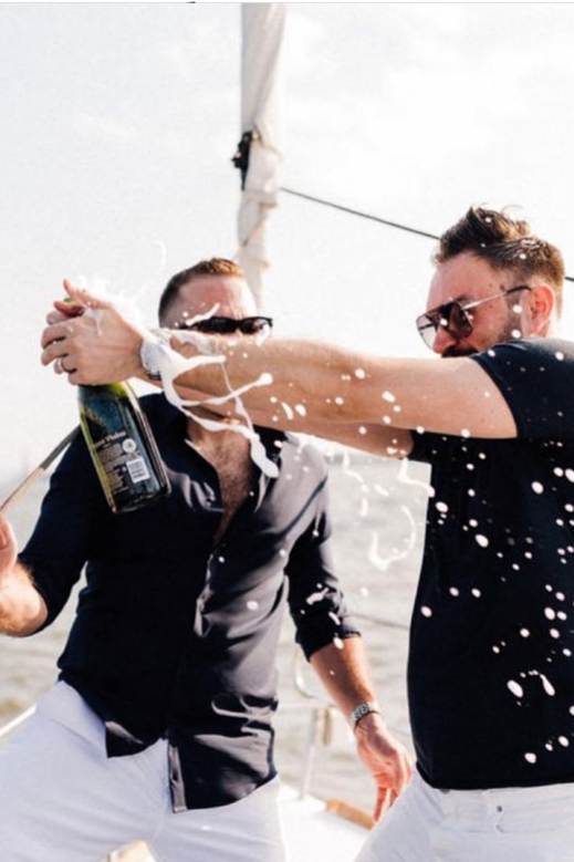 2 men in black shirts popping a champagne bottle during a private birthday cruise in NYC