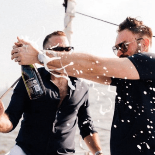 2 men in black shirts popping a champagne bottle during a small party boat rental in NYC
