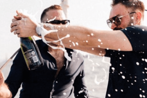 2 men in black shirts popping a champagne bottle during a small party boat rental in NYC