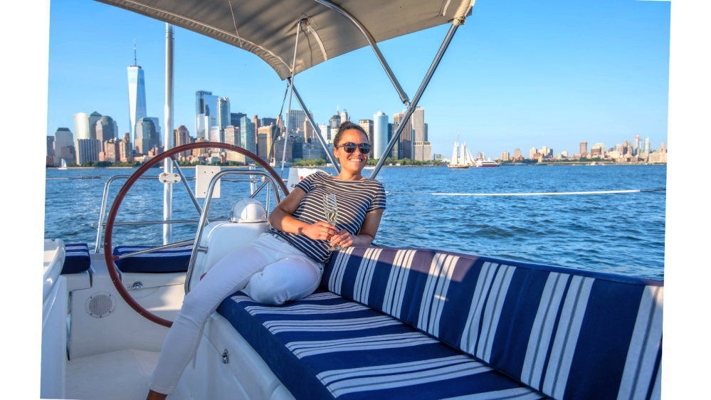 woman sitting on a blue and white striped cushions with a glass of champagne on a private boat charter in NYC with the financial district in the background