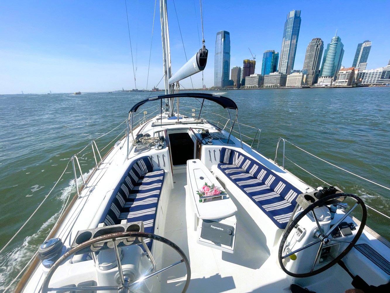 boat rent with blue striped deck cushions and two helms cruising through NYC waters with skyscrapers in the background