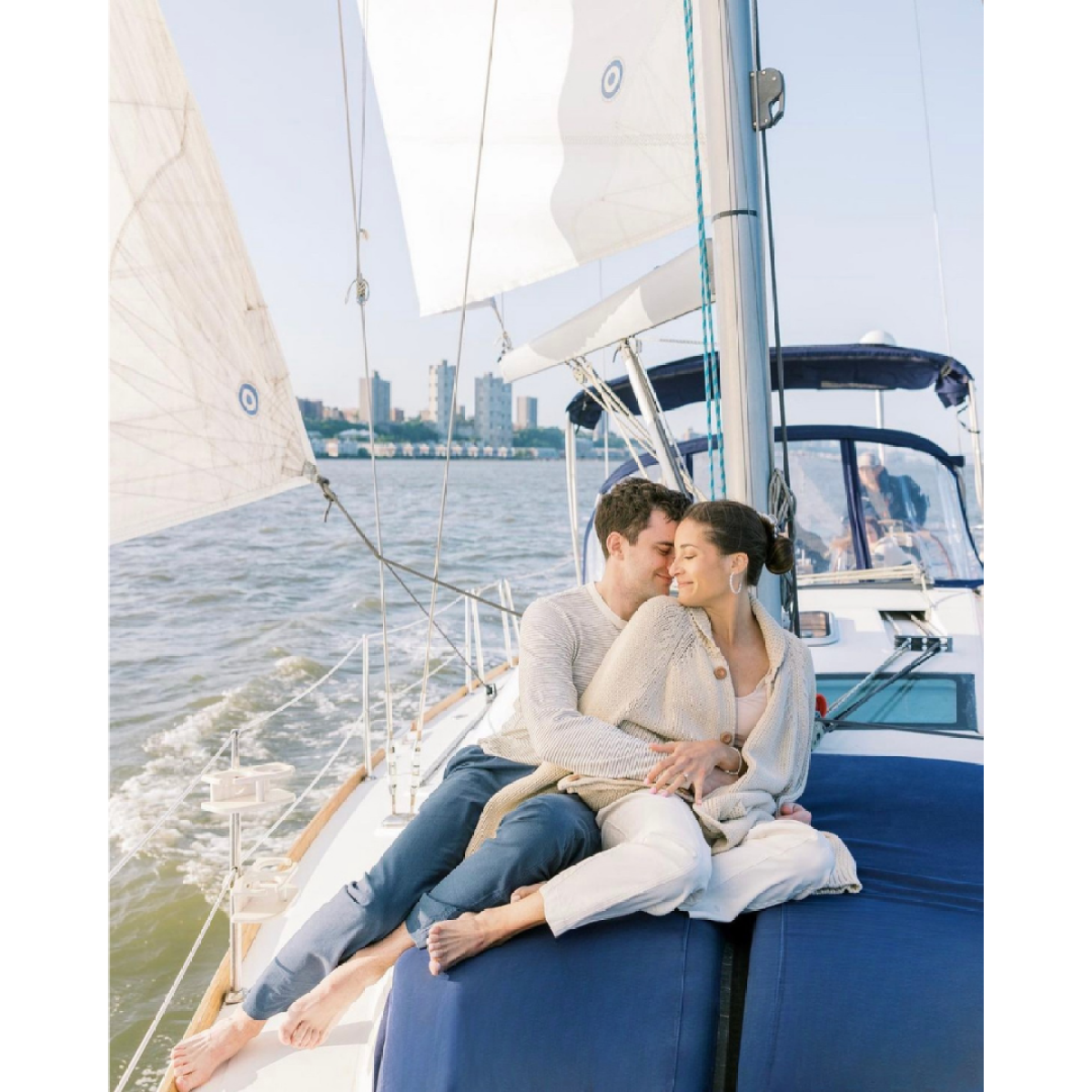 Couple cuddling on a sailboat with city skyline in the background during a boat proposal in NYC