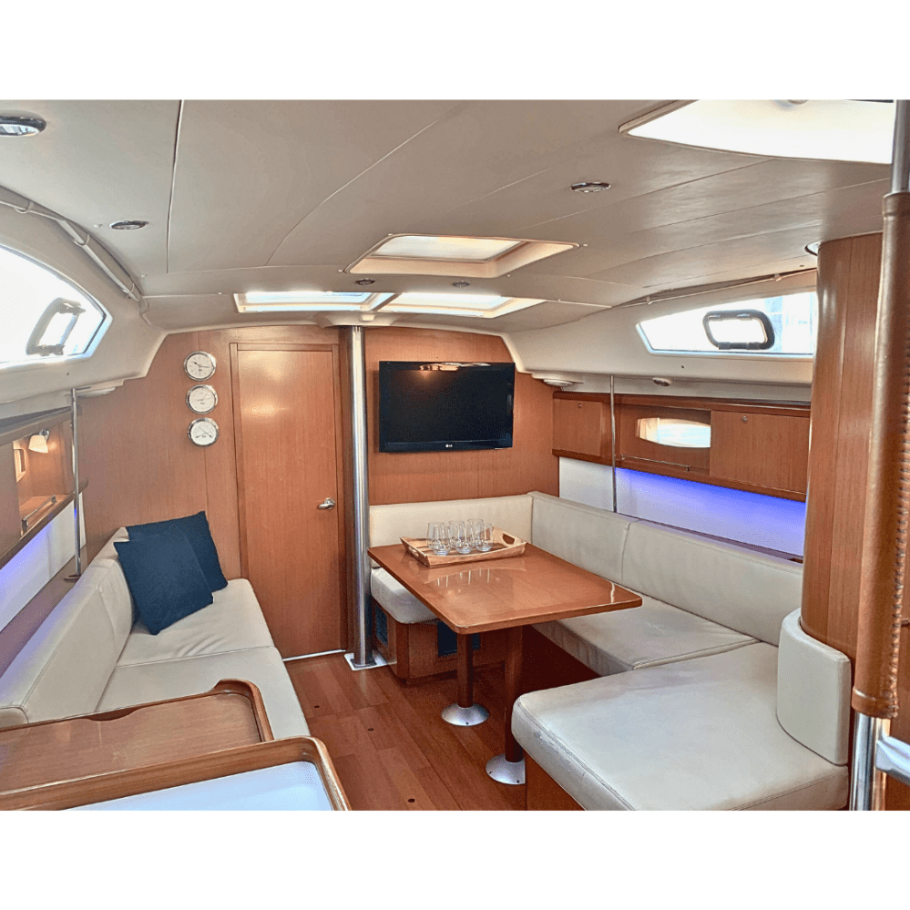 Interior of the cabin of a NYC sailboat rental with wood paneling, seating area, table, and wall-mounted TV.