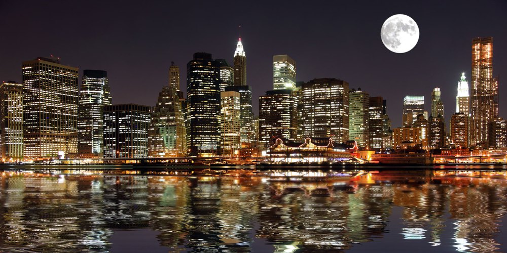Night skyline of a city with illuminated skyscrapers, a full moon, and reflections in the water.