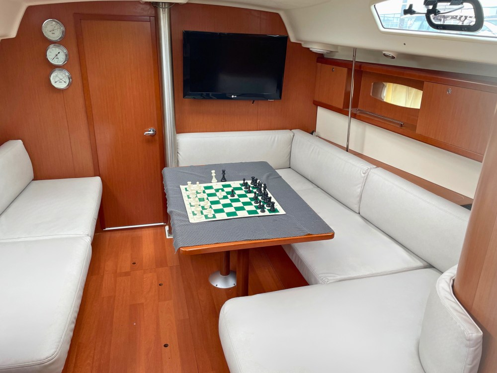 indoor cabin on NYC sailboat charter with C-shaped seating, chessboard on table, and wall-mounted TV, providing comfort during weather changes.