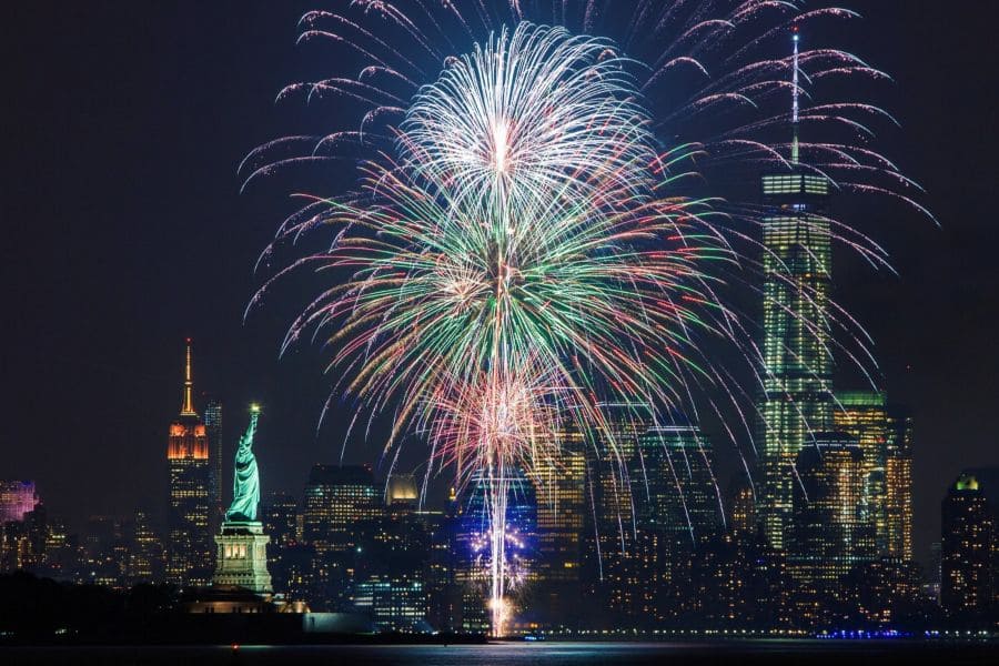 Fireworks over New York City skyline, featuring the Statue of Liberty and skyscrapers at night during a boat rental in NYC.