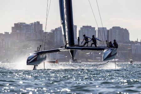 SailGP boat with crew navigating foils above water, NYC skyline in background, from the perspective of a private boat charter.