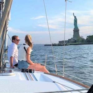 Two people sitting on a boat, with the Statue of Liberty in the background on a sunny day.