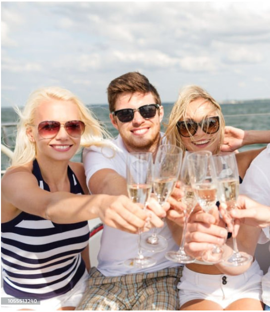 Birthday celebration on private sailboat with champagne, smiling and wearing sunglasses, with the New York Harbor in background