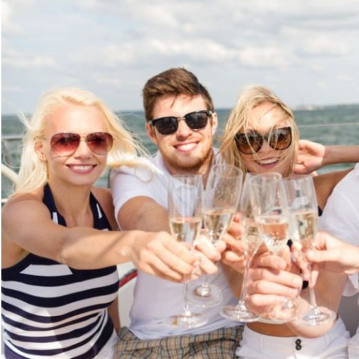 Three people on an after work boat hire in New York toasting with champagne glasses, smiling and wearing sunglasses.