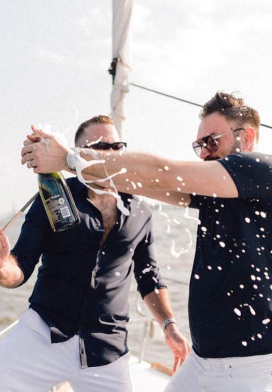 Two men on a boat charter in NYC celebrating a bachelor party with a spraying champagne bottle.
