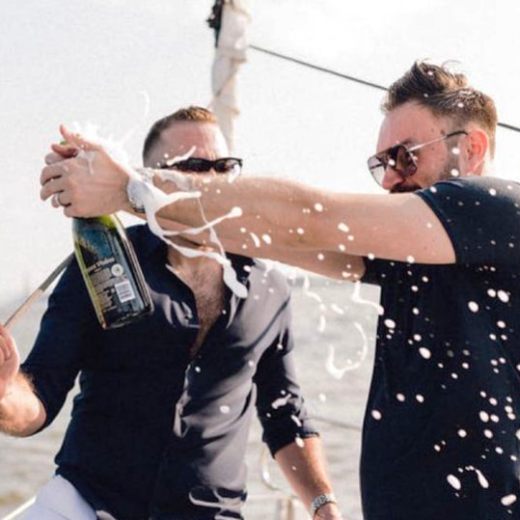 Two men on a boat charter in NYC celebrating a bachelor party with a spraying champagne bottle.