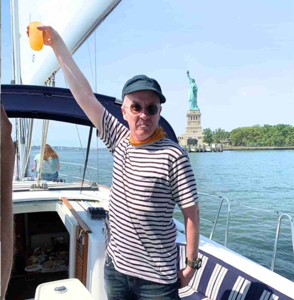 Person on a boat charter in NYC raising a drink with the Statue of Liberty in the background on a sunny day.
