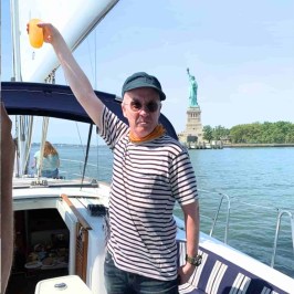 Person on a boat charter in NYC raising a drink with the Statue of Liberty in the background on a sunny day.