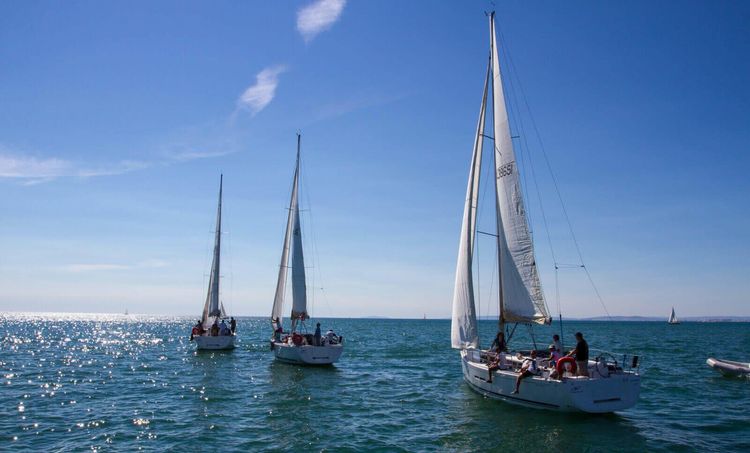 Three sailboats on a sunny day in a calm sea with clear blue sky.
