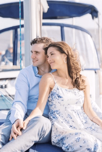Couple sitting on a boat charter in NYC, smiling and holding hands with blue sky background.